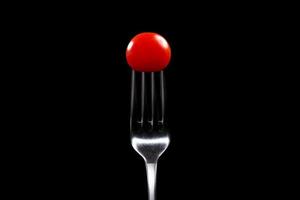garfo com close-up de tomate cereja. imagem isolada em um fundo preto. foto macro. conceito de cozinha