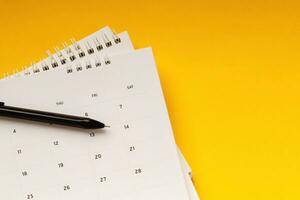 agenda do mês do calendário para fazer reuniões de compromisso ou gerenciar o cronograma a cada dia deitada e caneta em fundo amarelo para planejar o trabalho e o conceito de viagem. foto