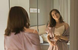 feliz manhã retrato. atraente jovem mulher olhando dentro espelho às dela apartamento - despertar acima e Novo dia foto