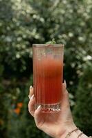 limonada com gelo dentro fêmea mão em vegetação fundo foto