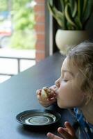 uma pequeno menina alegremente come uma rosquinha dentro uma cafeteria foto