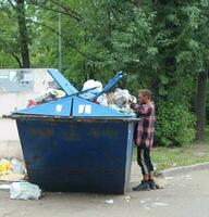 afundou Petersburgo Rússia - 08 17 2023 muito ruim sem teto vagabundo perto a lixo latas olhando para esvaziar garrafas e sobras Comida. a problema do sem teto pessoas durante a econômico crise foto