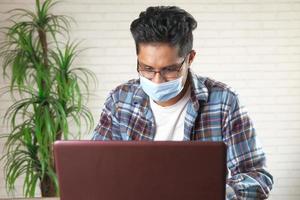 jovem asiático com máscara facial trabalhando em um laptop foto