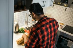 indiano ou latino homem cozinhando café da manhã enquanto em pé às a cozinha às lar, traseiro Visão foto