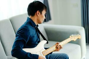 guitarrista jogando guitarra em sofá às casa praticando guitarra às casa relaxar de jogando amarrado instrumentos. foto