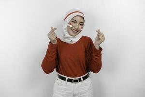 uma jovem ásia mulher vestindo uma vermelho topo e branco hijab sente nacionalismo, formas coração gesto expressa dela amor para Indonésia. da indonésia independência dia conceito. foto