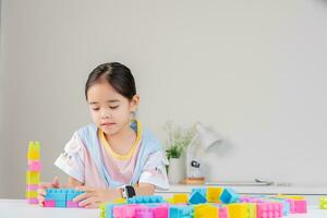 pequeno menina é feliz jogando colorida quadra quebra-cabeças. dentro a branco quarto foto