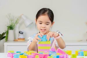 pequeno menina é feliz jogando colorida quadra quebra-cabeças. dentro a branco quarto foto