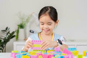 pequeno menina é feliz jogando colorida quadra quebra-cabeças. dentro a branco quarto foto