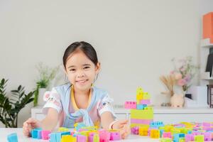 pequeno menina é feliz jogando colorida quadra quebra-cabeças. dentro a branco quarto foto