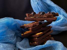 peças do chocolate com nozes e passas de uva em uma Sombrio fundo foto