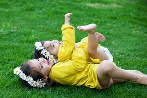 lindo pequeno irmãs vestido dentro amarelo jogando e tendo Diversão ao ar livre. felicidade conceito. família conceito foto