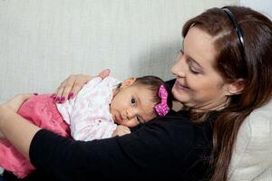 retrato do uma doce 1 mês bebê menina com dela jovem mãe às lar. maternidade conceito. família amor conceito. foto