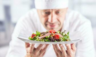 chefe de cozinha dentro a cozinha do a hotel ou restaurante segurando prato com Comida antes servindo foto