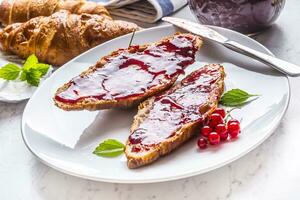 saboroso café da manhã com vermelho groselhas marmelada croissants manteiga e hortelã folhas foto