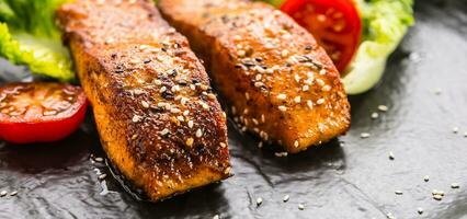 delicioso grelhado assado salmão filetes ou bifes com sésamo tomates e alface salada. foto