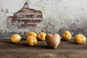 Batata vermelha em forma de coração entre batatas brancas em fundo vintage foto