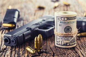 arma de fogo e dinheiro. 9 milímetros pistola arma de fogo balas espalhado e lista dólar notas em rústico carvalho mesa foto