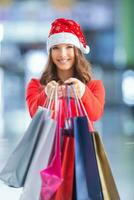 Natal compras. atraente feliz menina com crédito cartão e compras bolsas dentro santa chapéu foto