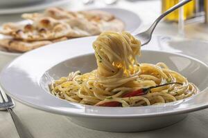 espaguete aglio e olio girado em uma garfo levando uma bocado parte do massa Fora do a prato foto