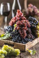 suculento cachos do uvas dentro uma de madeira caixa, vermelho vinho dentro a fundo foto