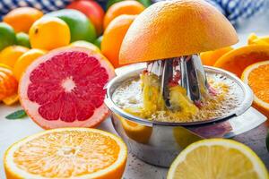 preparação do laranja uva ou multivitamínico suco, mãos aperto suco em uma manual metal espremedor cercado de fresco tropical fruta foto