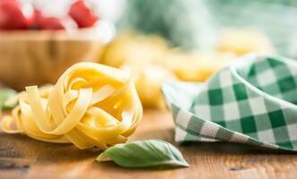 italiano massa tagliatelle em mesa com manjericão e tomates foto