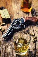 vidro do uísque conhaque ou bourbon com revólver e balas em de madeira mesa foto