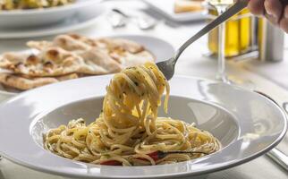 mão com uma garfo fiação espaguete aglio e olio peperoncino a partir de uma prato dentro uma restaurante foto