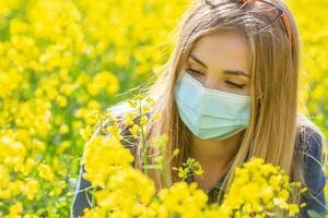 alérgico Loiras menina dentro uma protetora mascarar parece às a amarelo flor sentado em uma Prado foto