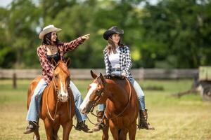 dois vaqueiras patrulhando a rancho passeio seus cavalos com 1 apontando em a horizonte foto