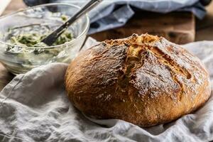 recentemente cozido pão pão em uma linho toalha Próximo para uma tigela do erva manteiga foto