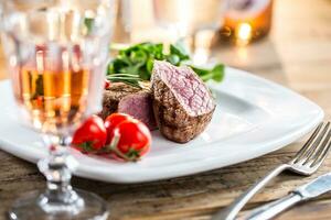 carne bife. suculento carne bife. gourmet bife com legumes e vidro do rosa vinho em de madeira mesa foto