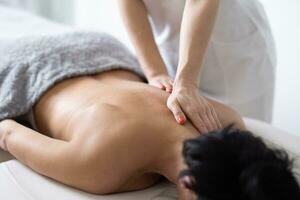 ombro lâmina e costas massagem do demale massagista para uma fêmea cliente deitado cabeça baixa em uma massageando mesa foto