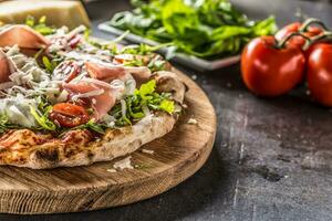 italiano pizza com prosciutto Rúcula tomates e parmesão em de madeira volta borda foto