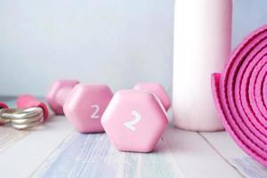 haltere cor-de-rosa, tapete para exercícios e garrafa de água no fundo branco foto