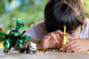 fechar acima ásia menina 5-6 ano velho criança jogando com Lego tijolos ou brinquedo às lar, ásia meninas relaxar com jogando tijolo blocos em de madeira mesa e apreciar jogando brinquedos. foto