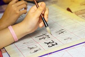ásia alunos prática a arte do chinês caligrafia de escrevendo chinês personagens, a palavra ni hao , que significa Olá em papel. suave e seletivo foco. foto