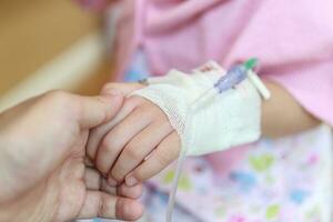 mãe segurando criança mão com salina iv solução dentro hospital foto