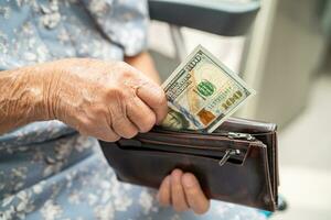 ásia Senior mulher segurando e contando nos dólar notas dinheiro dentro bolsa. pobreza, salvando problema dentro aposentadoria. foto