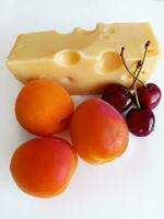 queijo, damascos e cerejas em uma branco fundo foto