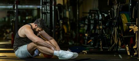 caucasiano homem é voltado para overtraining síndrome depois de exercite-se dentro Academia com Sombrio fundo para exercício e ginástica conceito foto