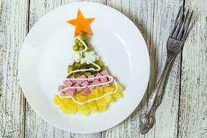 Natal árvore a partir de uma salada olivier dentro prato em uma branco de madeira mesa. topo Visão com uma cópia de espaço foto