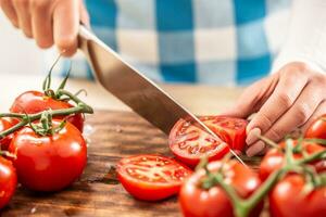 detalhe do fêmea mãos corte uma tomate de uma faca em uma cortar borda com Mais fresco tomates por aí foto