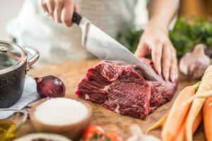 jovem dona de casa fatiamento fresco carne bife. fêmea mãos preparando almoço do carne e legumes foto