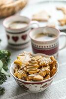 uma tigela cheio do Natal Pão de gengibre em a mesa conduziu a advento guirlanda e dois copos com café, soco ou chá foto