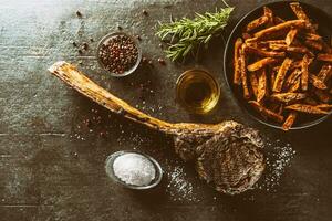 grelhado carne tomahawk bife com doce batata fritas sal especiarias Oliva óleo e alecrim em rústico borda - topo do Visão foto