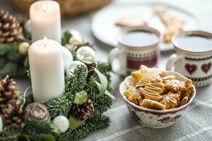 uma tigela cheio do Natal Pão de gengibre em a mesa conduziu a advento guirlanda e dois copos com café, soco ou chá foto