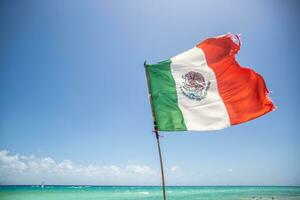 mexicano bandeira parcialmente rasgado de a vento sopro a partir de a turquiose Caribe mar foto