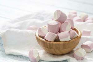 de madeira tigela cheio do Rosa e branco marshmallows com alguns espalhados por aí em uma branco mesa pano foto